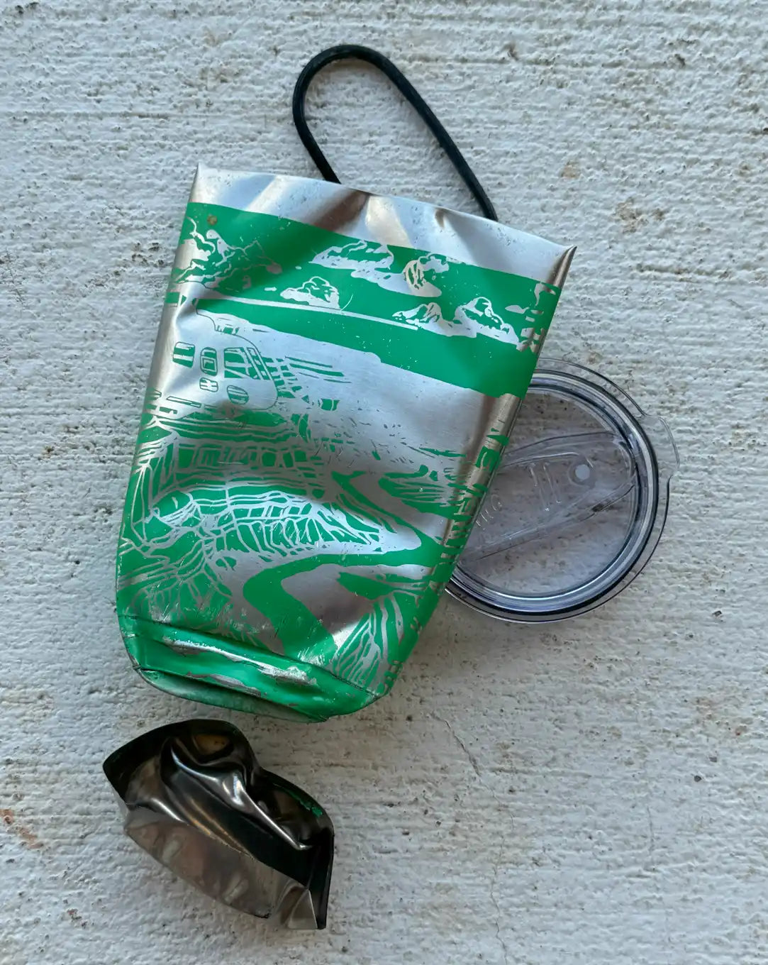 Crushed green and silver insulated tumbler with lid and broken piece.